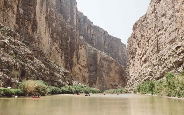 a group of kayaks are paddled along a river surrounded by high canyon walls